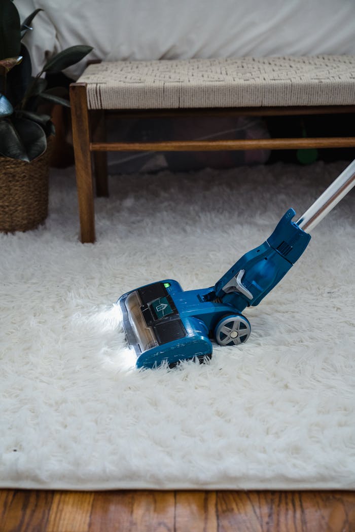 Modern blue vacuum cleaner on a white fur carpet in a cozy indoor setting.